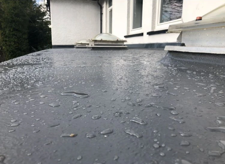 Wet flat rooftop with water droplets and a dome skylight near a white building wall.