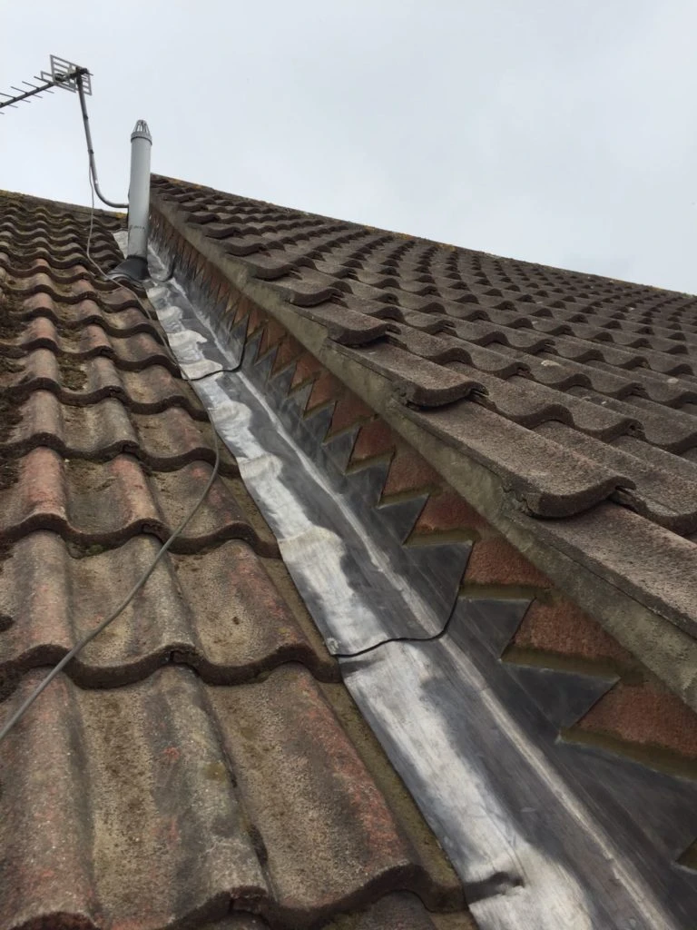 Sloped roof with weathered brown tiles, metal flashing along the ridge and a TV antenna attached.