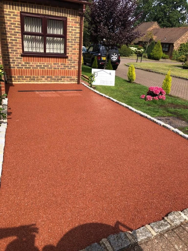 Newly laid red resin driveway bordered with stone edging in front of a brick house with a window.