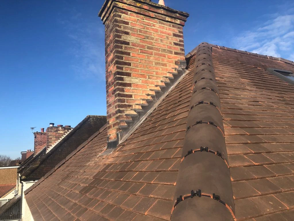 Sloped roof with brown shingles and brick chimneys under a partly cloudy blue sky.