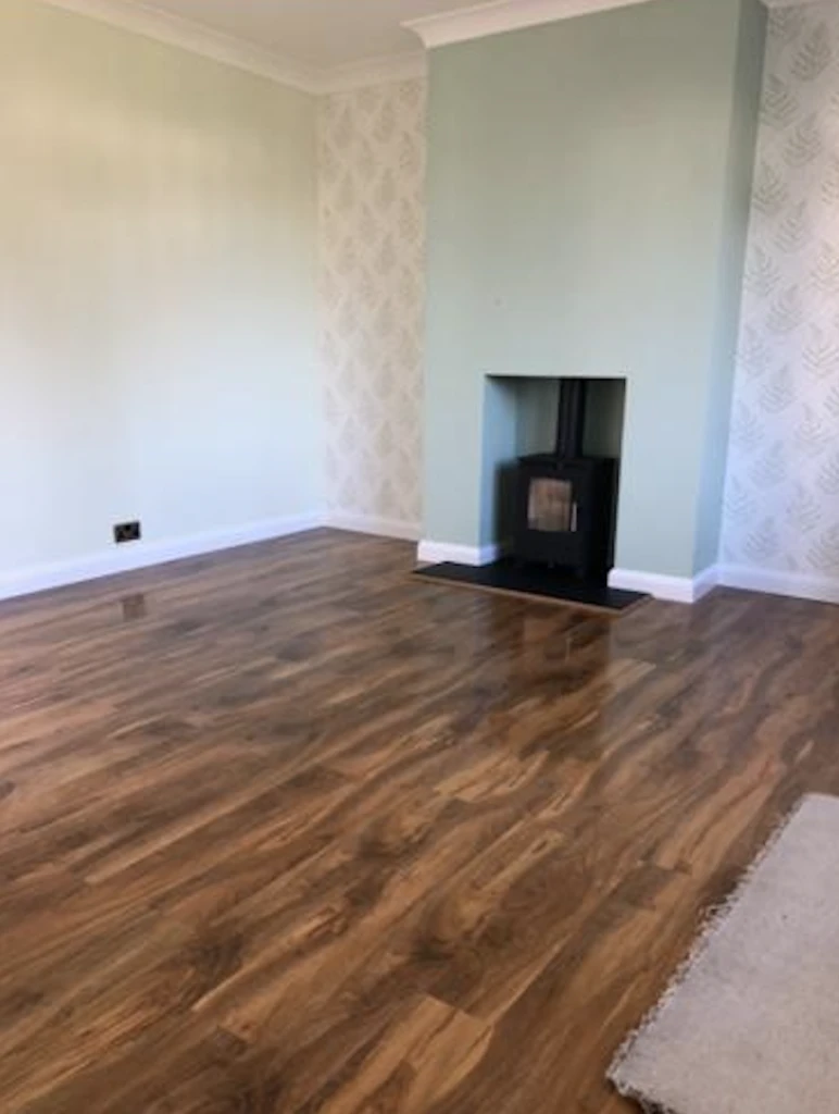 Empty room with polished wood floor, pale green walls, and a black wood stove in the fireplace.