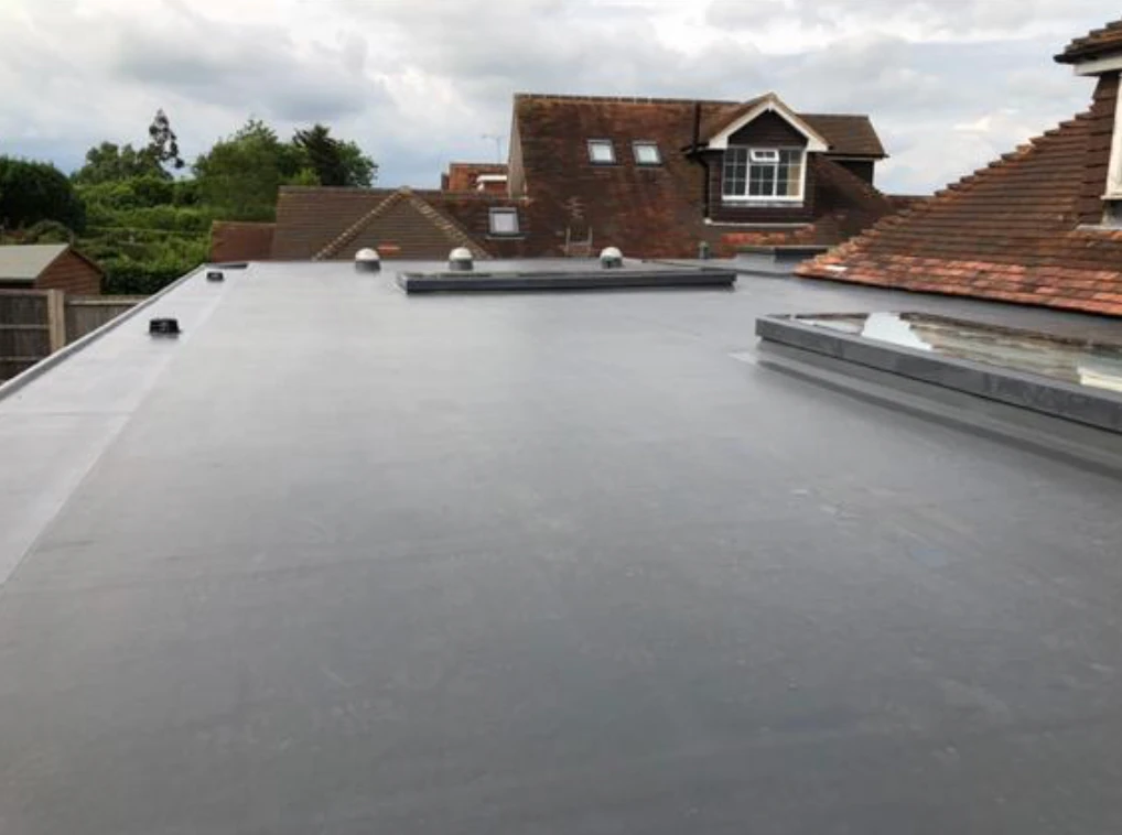 Flat roof with gray waterproof membrane on a residential building under a cloudy sky.