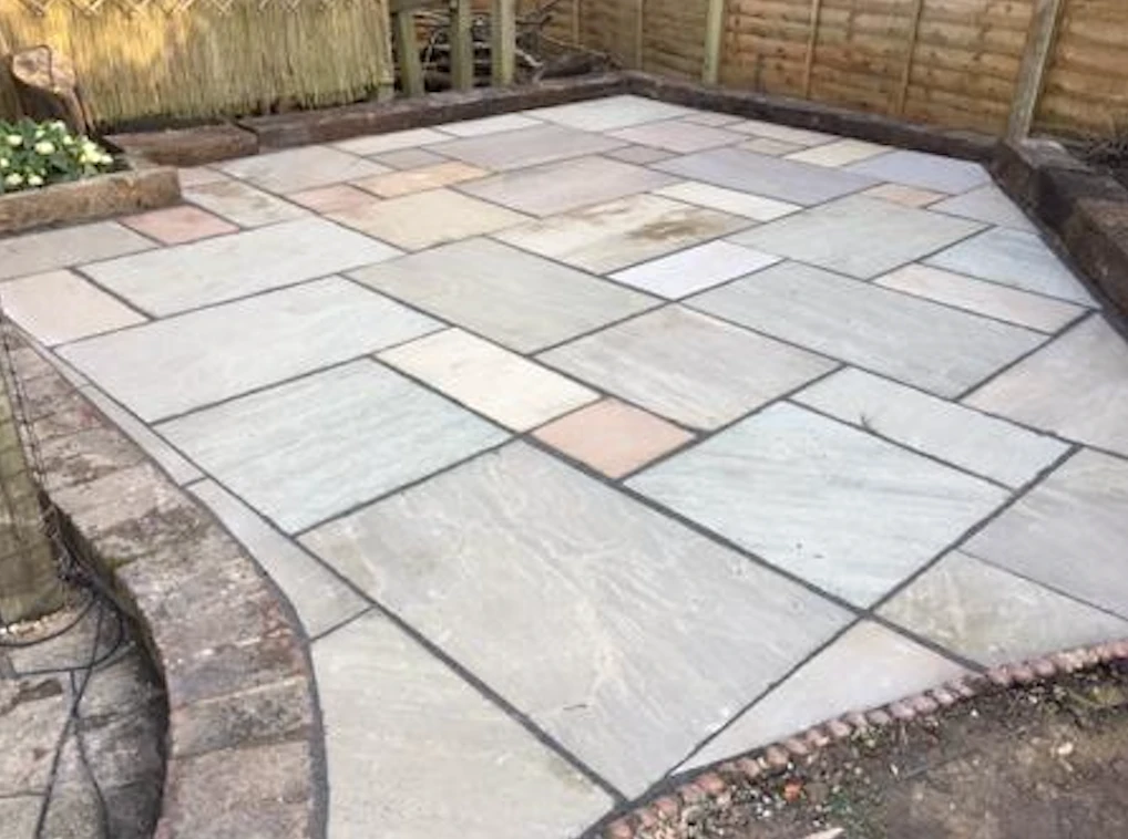 Newly installed patio with rectangular stone slabs in varying shades surrounded by a brick edge.
